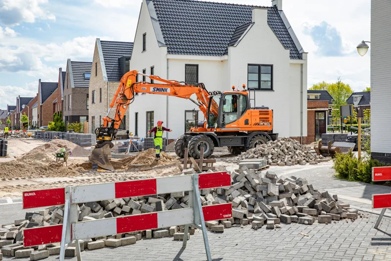 Graafmachine en bestratingsmateriaal in een woonstraat met nieuwbouwwoningen.
